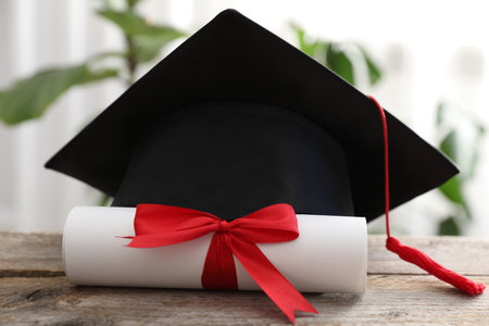 Diploma and graduation hat on wooden table indoors, closeupの写真素材