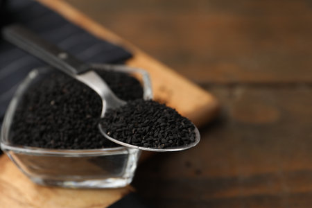 Aromatic black caraway in glass bowl and spoon on wooden table, closeup. Space for textの写真素材