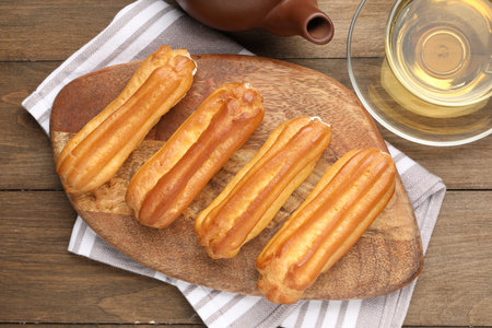 Tasty eclairs and tea on wooden table, flat lay