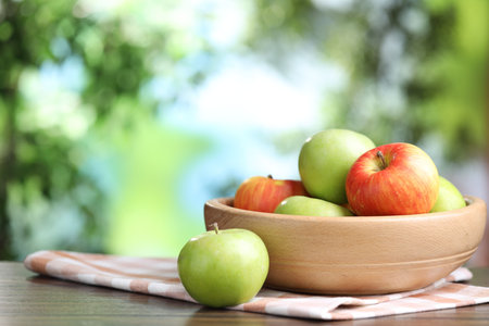 Fresh apples and bowl on wooden table against blurred green background, closeup. Space for textの写真素材