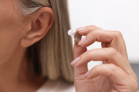 Senior woman putting hearing aid into ear at home, closeupの写真素材