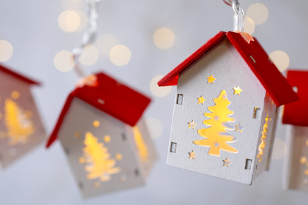 Festive lights in shape of houses hanging against gray background with blurred lights, closeup....