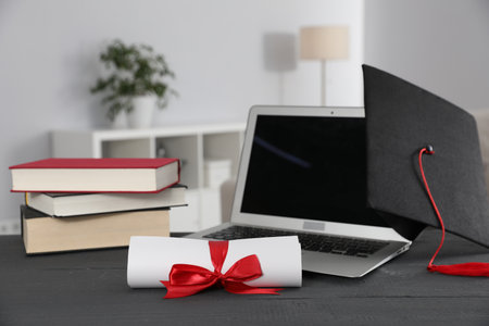 Diploma, graduation hat, laptop and books on gray wooden table indoorsの写真素材