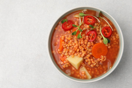 Delicious lentil soup with vegetables in bowl on light gray table, top view. Space for textの写真素材
