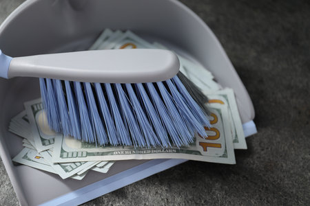 Dustpan with broom and dollar banknotes on gray surface, closeupの写真素材