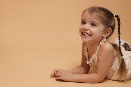 Happy little girl with pigtails on beige background. Space for textの写真素材