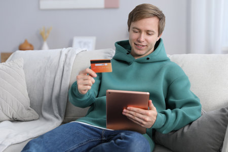Young man making online payment with tablet and credit card indoorsの写真素材