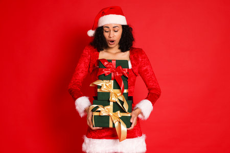 Surprised woman in Mrs Claus costume with Christmas gifts on red background