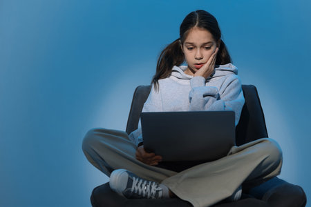 Cyber danger. Frightened girl using laptop on blue background, space for textの写真素材
