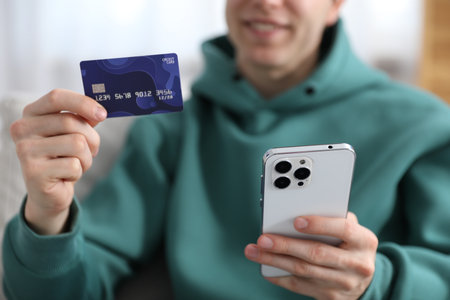 Young man making online payment with phone and credit card indoors, closeupの写真素材