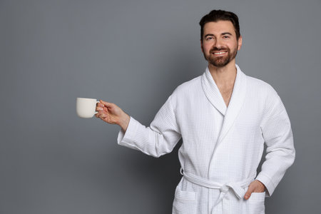 Man in bathrobe with cup of coffee on gray background. Space for textの写真素材