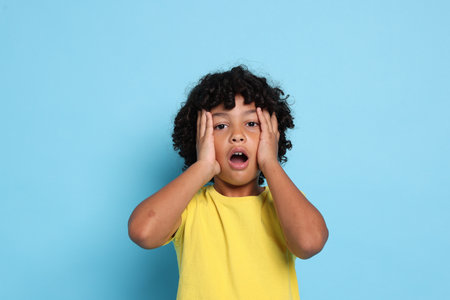 Portrait of surprised little boy on light blue background