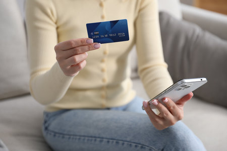 Woman making online payment with phone and credit card indoors, closeupの写真素材