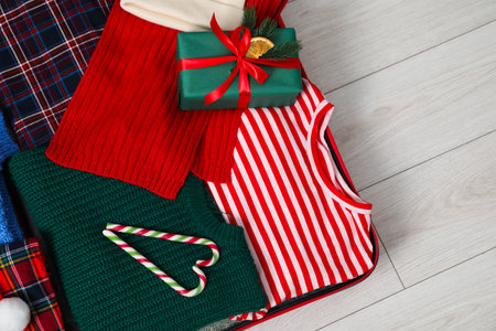 Christmas vacation. Suitcase with clothes, gift box and candy canes on floor indoors, top view