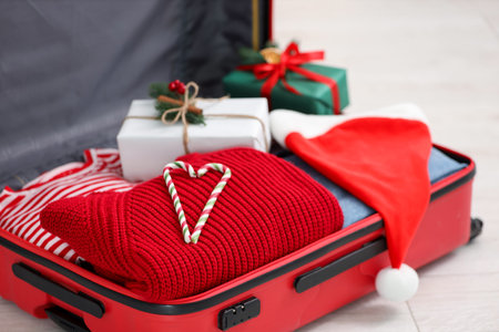 Christmas vacation. Suitcase with Santa hat, clothes, gift boxes and candy canes on floor indoors, closeupの写真素材