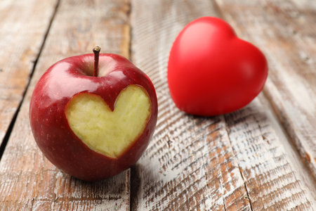 Ripe apple with carved heart and heart model on color wooden table, closeupの写真素材
