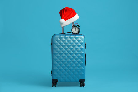 Christmas vacation. Suitcase with red Santa hat and alarm clock on light blue backgroundの写真素材