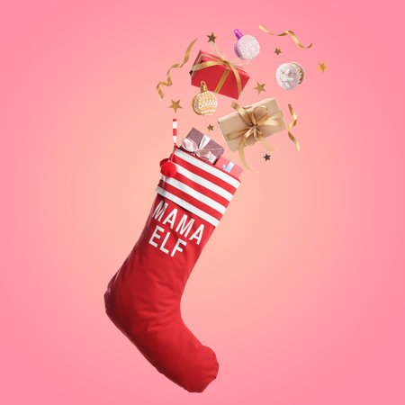 Gift boxes, Christmas cookies and festive decor falling into red stocking on pink backgroundの写真素材