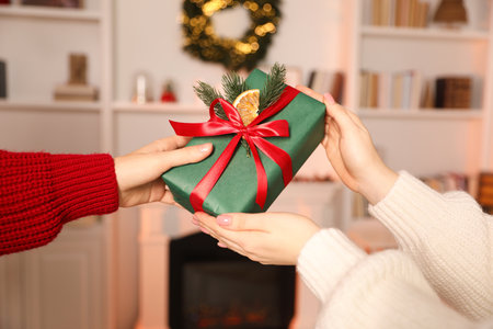 Merry Christmas and Happy New Year. Woman giving gift box to her friend indoors, closeup