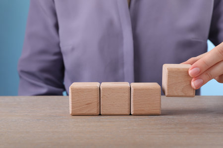 Woman putting cube next to others on wooden table, closeup. Space for designの写真素材
