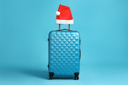 Christmas vacation. Suitcase with red Santa hat on light blue backgroundの写真素材