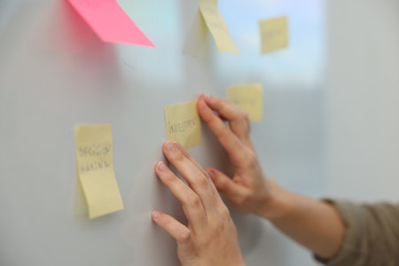 Woman sticking note with word Investment on whiteboard in office, closeupの写真素材