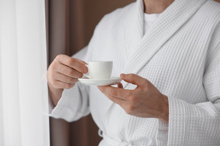 Man in bathrobe with cup of coffee indoors, closeupの写真素材