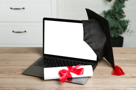 Diploma, graduation cap and laptop on wooden table indoors, closeupの写真素材