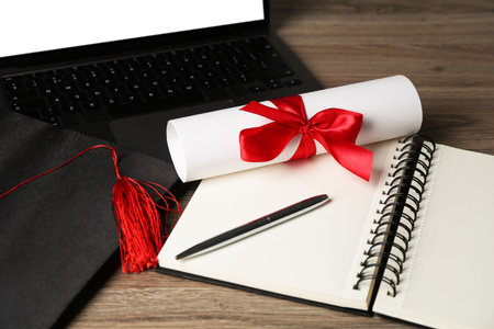 Diploma, graduation cap, notepad, pen and laptop on wooden table, closeupの写真素材