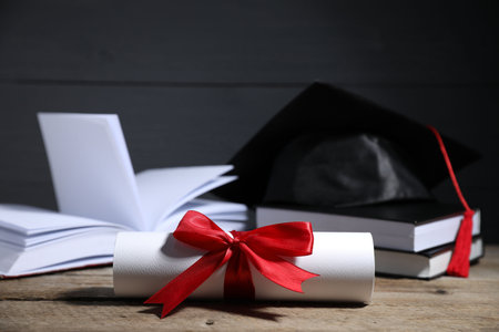 Diploma, graduation hat and books on wooden table, selective focusの写真素材