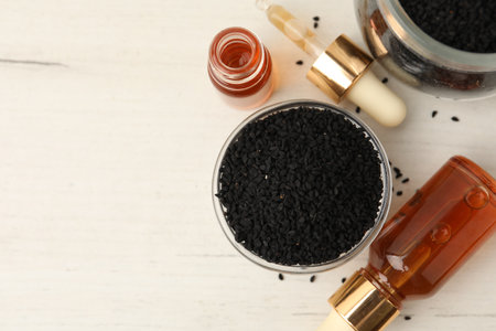 Black cumin seeds and bottles of essential oil on light wooden table, flat lay. Space for textの写真素材