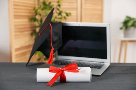Diploma, graduation hat and laptop on gray wooden table indoors, selective focusの写真素材