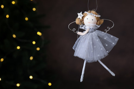 Christmas decor. Fairy doll hanging on black background with blurred lights, closeup. Space for textの写真素材