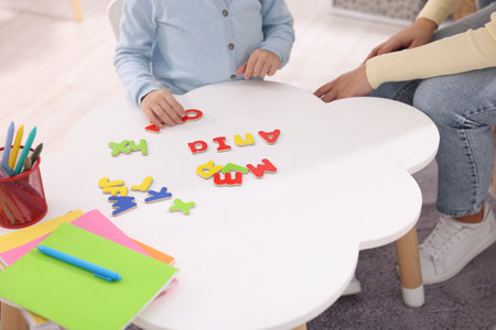 Mother teaching her daughter alphabet at white table indoors, closeupの写真素材