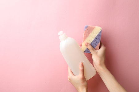 Woman holding sponge and dish soap on pink background, top view. Space for textの写真素材