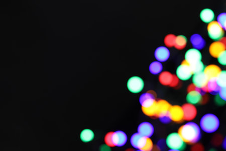 Blurred view of bright Christmas lights on dark background, bokeh effect. Space for textの写真素材