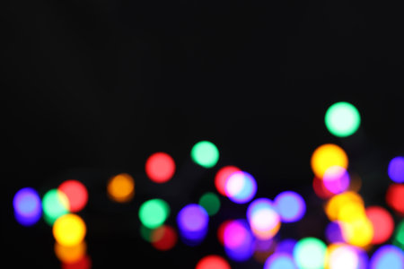 Blurred view of bright Christmas lights on dark background, bokeh effect. Space for textの写真素材