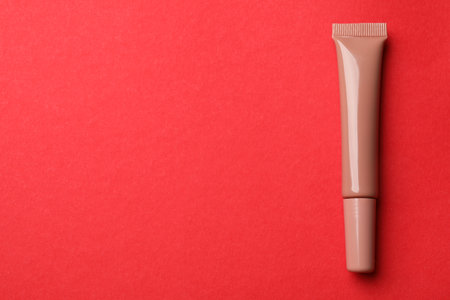 Beautiful nude lip gloss on red background, top view. Space for textの写真素材