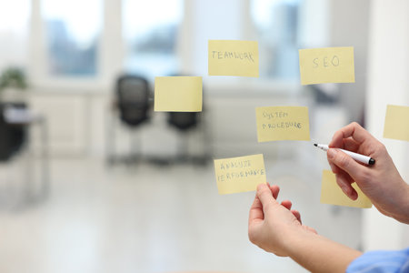 Woman sticking note with text Analyze Performance on glass board in office, closeup. Space for textの写真素材