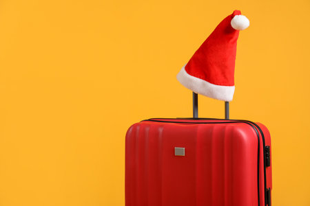 Christmas vacation. Red suitcase with Santa hat on orange background, space for textの写真素材