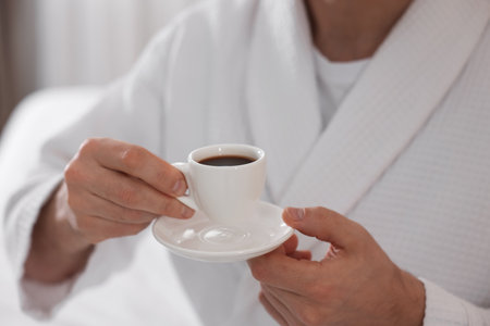 Man in bathrobe with cup of coffee indoors, closeupの写真素材