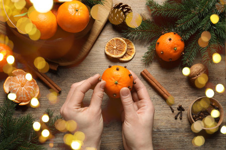 Woman decorating fresh tangerine with cloves at wooden table, top view. Bokeh lightsの写真素材