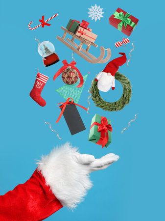 Christmas decor and gift boxes levitating above Santa's hand on pastel blue background, closeup. Festive magicの写真素材