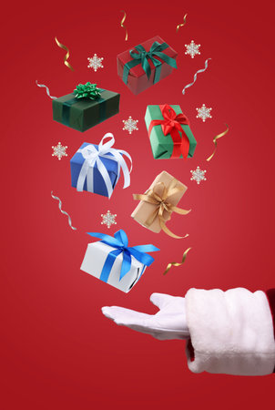 Gift boxes levitating above Santa's hand on red background, closeup. Christmas magicの写真素材