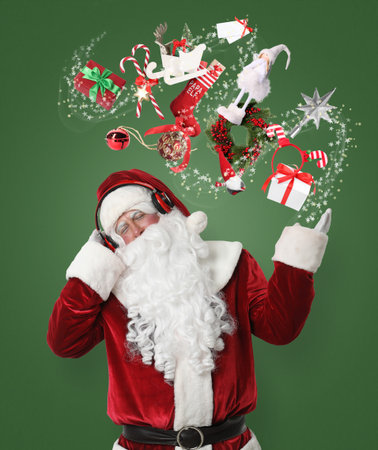 Santa Claus levitating Christmas decor and gift boxes while listening to music on green background. Festive magicの写真素材