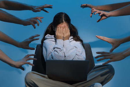 Cyber danger. Frightened girl using laptop while hands reaching towards her on blue backgroundの写真素材