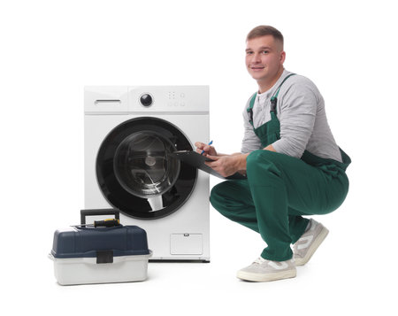 Smiling repairman in uniform with pen, clipboard, toolbox and washing machine on white backgroundの写真素材