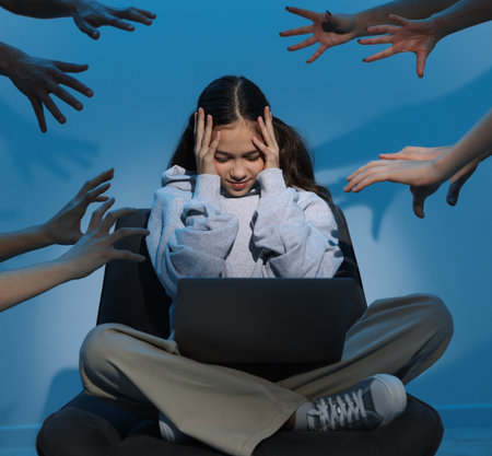 Cyber danger. Frightened girl using laptop while hands reaching towards her on blue backgroundの写真素材