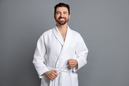 Man tying belt of bathrobe on gray backgroundの写真素材