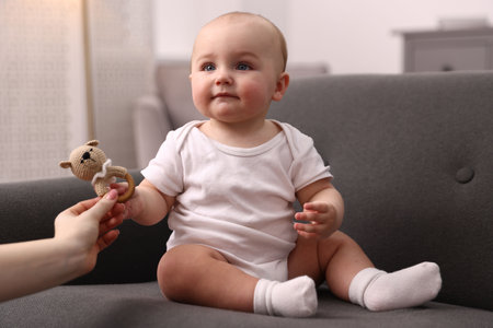 Mother giving rattle toy to her cute little baby on sofa at home, closeupの写真素材